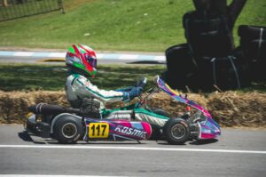 Un pilote de karting roulant à toute vitesse sur une piste extérieure par une journée ensoleillée avec un équipement de sécurité.