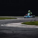 Photo dynamique d'un pilote de karting filant à toute vitesse dans une courbe de piste, mettant en valeur le frisson du sport automobile.