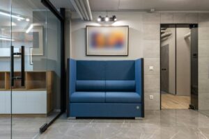 Salon de bureau contemporain spacieux avec un canapé bleu, des portes vitrées et une décoration minimaliste.