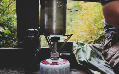 Cuisinière de camping avec casserole et bouteille d'eau sur table en forêt